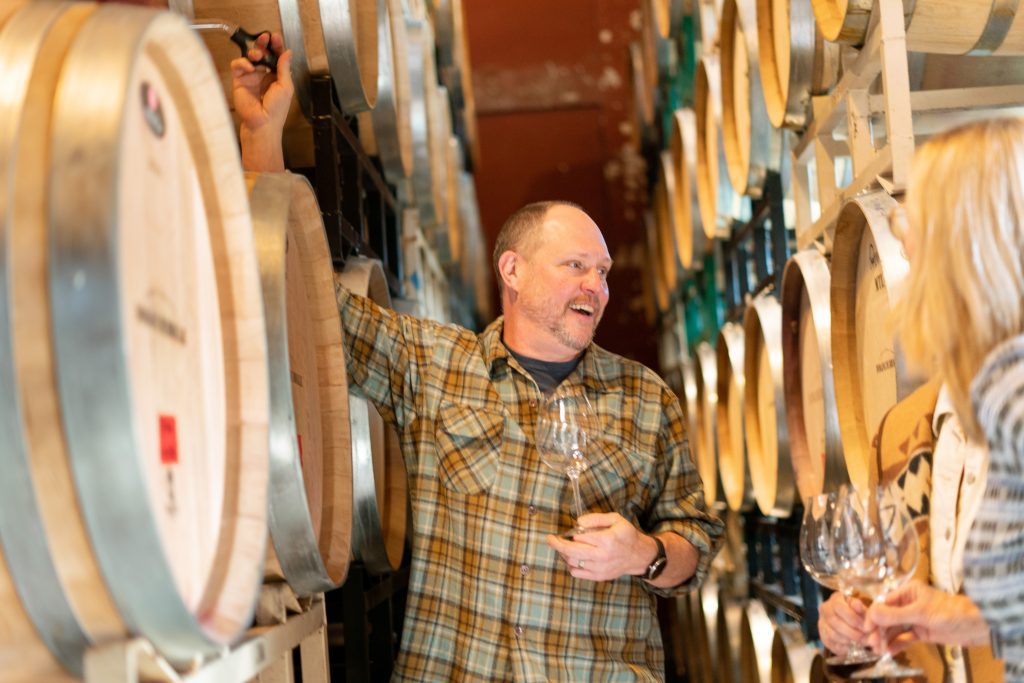 Winemaker in a cellar, using a wine thief to extract a sample. from a wine barrel.