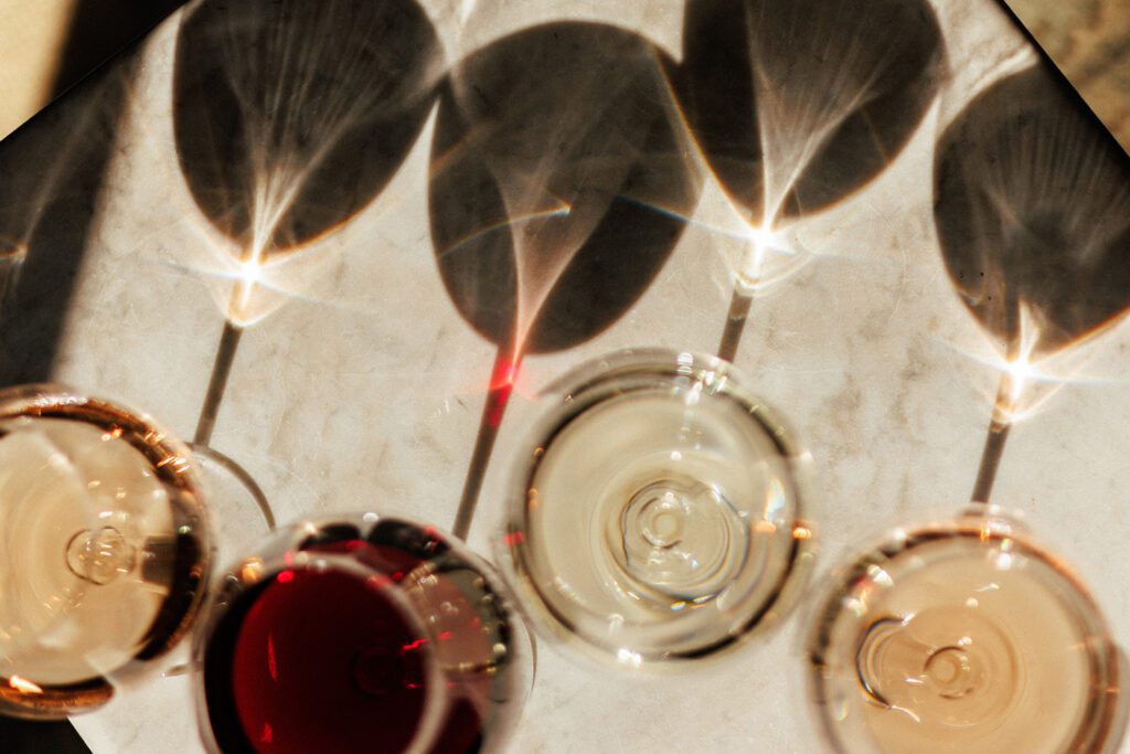 Glasses of wine of varying colors with shadows on a table.